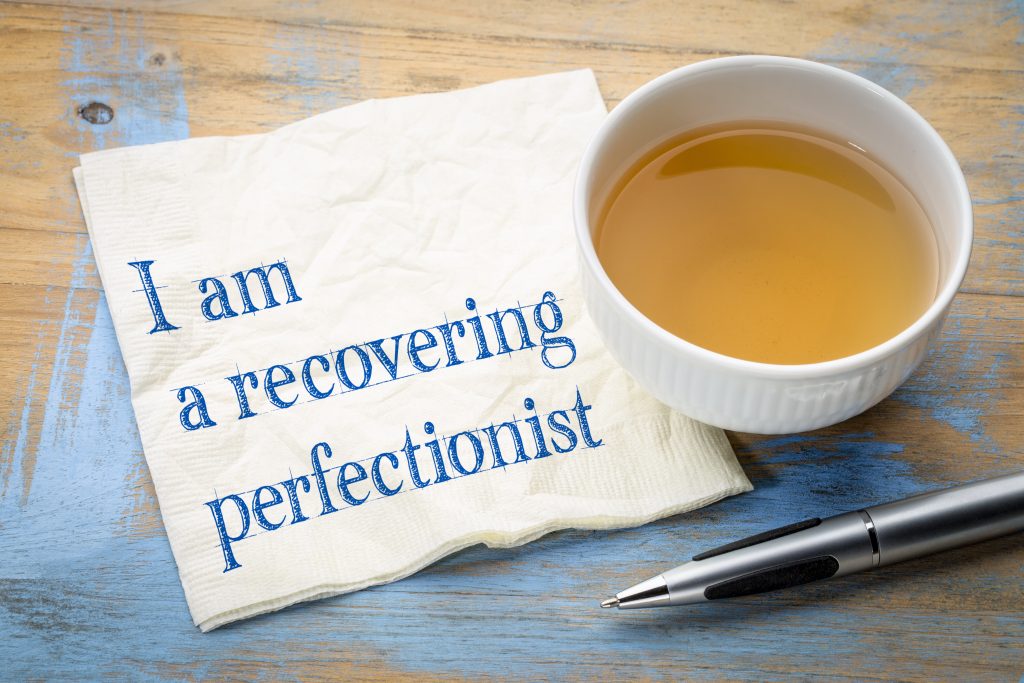 Eine Tasse mit Tee steht neben einem Blatt und einem Kugelschreiber. Auf dem Blatt steht: „I am a recovering perfectionist.“ 