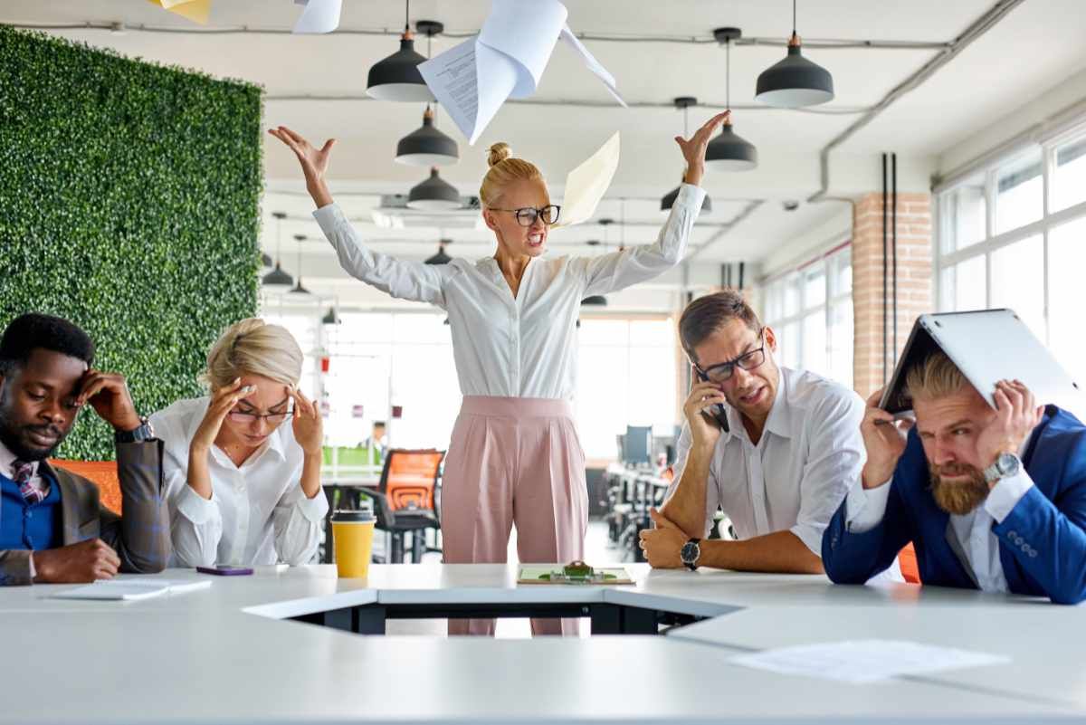 Symbolbild bei sich bleiben: Im Meeting wirft eine Frau verärgert Unterlagen in die Luft; die Mitarbeiter sind frustriert und genervt